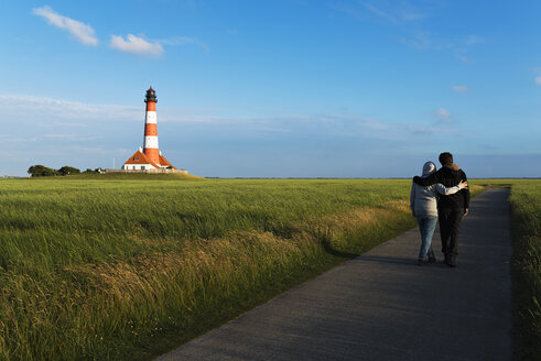 Deutschland, Westerhever, Paar spaziert am Leuchtturm entlang - MKFF00483