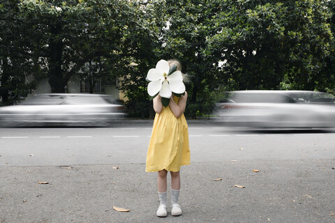 Mädchen im gelben Kleid versteckt ihr Gesicht hinter einer übergroßen weißen Magnolienblüte, lizenzfreies Stockfoto