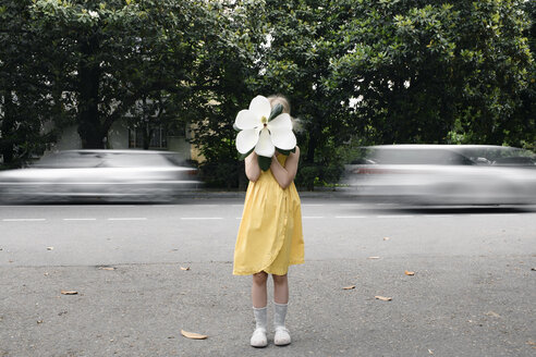 Girl wearing yellow dress hiding her face behind oversized white magnolia blossom - EYAF00086
