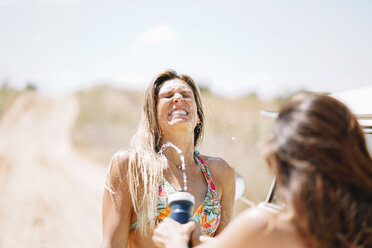 Zwei glückliche junge Frauen im Bikini spritzen Wasser - OCMF00361