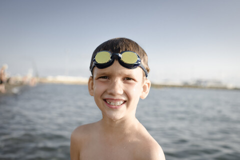 Porträt eines glücklichen Jungen mit Schwimmbrille am Meer, lizenzfreies Stockfoto
