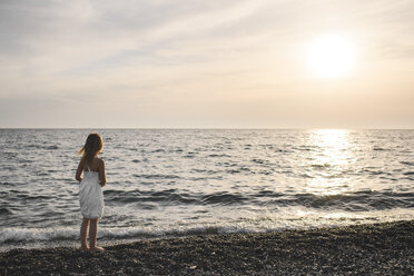 Little girl in white dress looking at sunset over the sea - EYAF00116