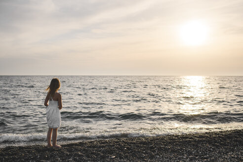 Kleines Mädchen im weißen Kleid mit Blick auf den Sonnenuntergang über dem Meer - EYAF00116