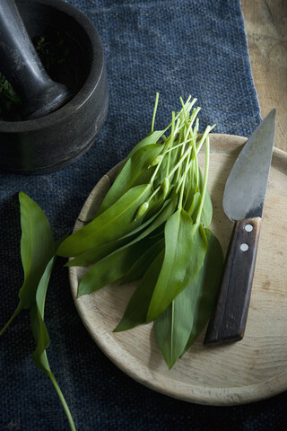 Ramson und Messer auf Holzbrett, Mörser und Schale mit Pinienkernen, lizenzfreies Stockfoto