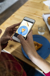 Person, die mit ihrem Smartphone ein Stück Pizza auf einem Teller fotografiert - GIOF06090