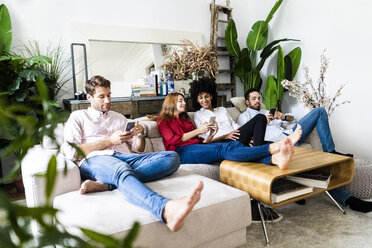 Friends sitting on couch, working casually together, using smartphones - GIOF06109