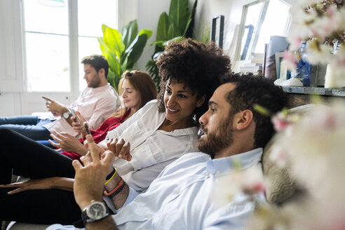 Freunde sitzen auf der Couch, arbeiten zwanglos zusammen und benutzen Smartphones - GIOF06111