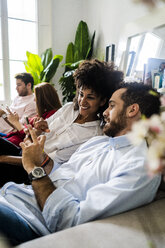 Friends sitting on couch, working casually together, using smartphones - GIOF06113