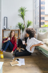 Lässige Geschäftsfrauen sitzen auf dem Boden, trinken Kaffee und arbeiten am Laptop - GIOF06135