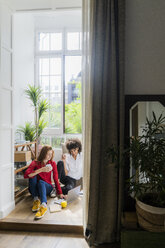 Casual businesswomen sitting on floor, drinking coffee, working on laptop - GIOF06138