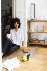 Relaxed woman sitting on floor of her flat, drinking coffee - GIOF06142