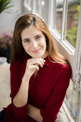 Portrait of a smiling woman, sitting on a bench at the window - GIOF06153