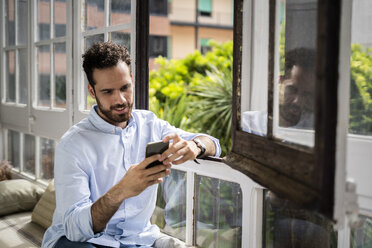 Young man sitting on bench at the window, using smartphone - GIOF06158