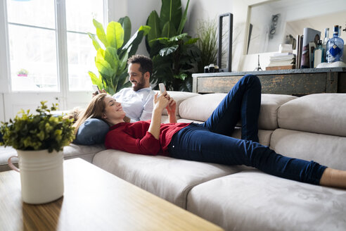 Pärchen auf der Couch liegend, mit ihren Smartphones - GIOF06164