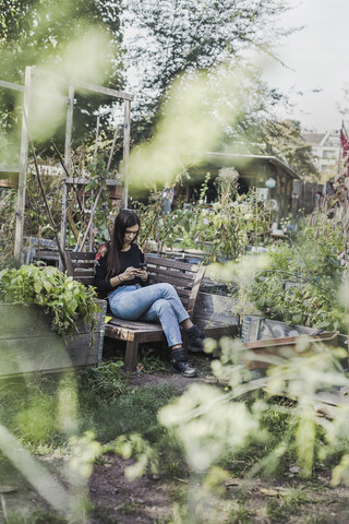 Frau benutzt Smartphone im städtischen Garten, lizenzfreies Stockfoto