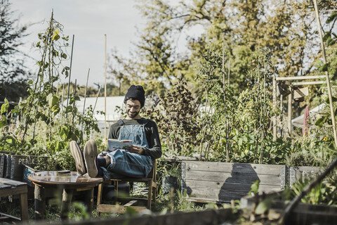 Lächelnder Mann, der in einem städtischen Garten ein Buch liest, lizenzfreies Stockfoto