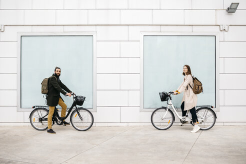 Porträt eines Mannes und einer Frau mit E-Bikes, die vor einem Gebäude stehen - JRFF02893