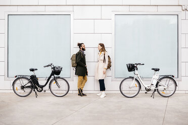 Mann und Frau mit E-Bikes stehen vor einem Gebäude und unterhalten sich - JRFF02894