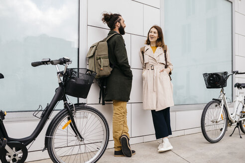 Mann und Frau mit E-Bikes stehen vor einem Gebäude und unterhalten sich - JRFF02895