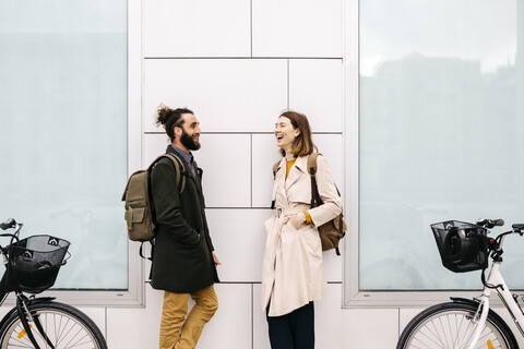Mann und Frau mit E-Bikes stehen vor einem Gebäude und unterhalten sich, lizenzfreies Stockfoto
