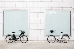 Zwei E-Bikes an einer weißen Wand mit zwei Fenstern - JRFF02899