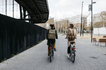 Rear view of couple riding e-bikes in the city talking to each other - JRFF02907