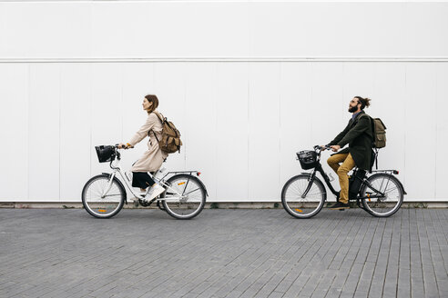 Ein Paar fährt mit einem E-Bike an einer weißen Wand in der Stadt entlang - JRFF02908