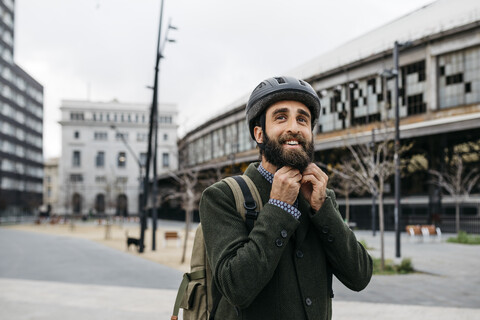 Porträt eines lächelnden Mannes, der in der Stadt einen Fahrradhelm aufsetzt, lizenzfreies Stockfoto