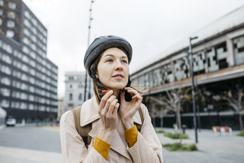 Portrait of woman putting on bicycle helmet in the city - JRFF02918