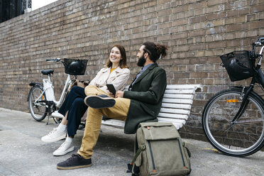 Ehepaar sitzt auf einer Bank neben E-Bikes und unterhält sich - JRFF02929