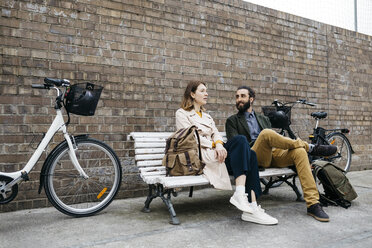 Couple sitting on a bench next to e-bikes talking - JRFF02930