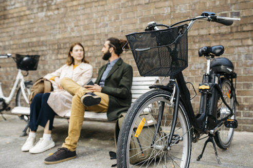 Ehepaar sitzt auf einer Bank neben E-Bikes und unterhält sich - JRFF02931
