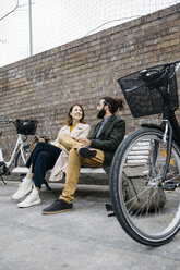 Couple sitting on a bench next to e-bikes talking - JRFF02933