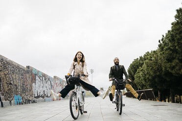 Carefree couple riding e-bikes on a promenade - JRFF02934