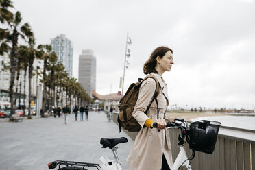 Woman with e-bike having a break on beach promenade - JRFF02938