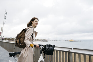 Lächelnde Frau mit E-Bike macht eine Pause auf der Strandpromenade - JRFF02939