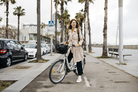 Lächelnde Frau mit E-Bike auf einer Promenade, lizenzfreies Stockfoto