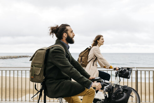 Couple riding e-bikes on beach promenade - JRFF02946