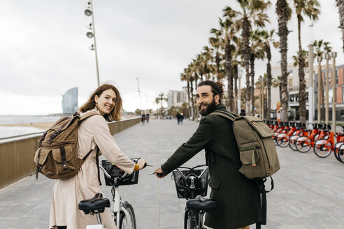 Lächelndes Paar mit E-Bikes auf der Strandpromenade - JRFF02949