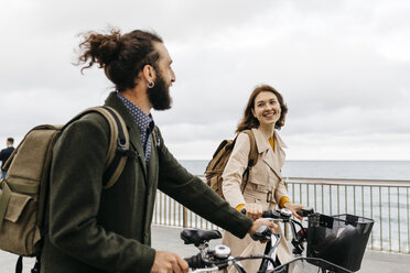 Lächelndes Paar mit E-Bikes auf der Strandpromenade - JRFF02951