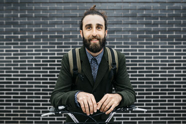Portrait of smiling man with e-bike at a brick wall - JRFF02961