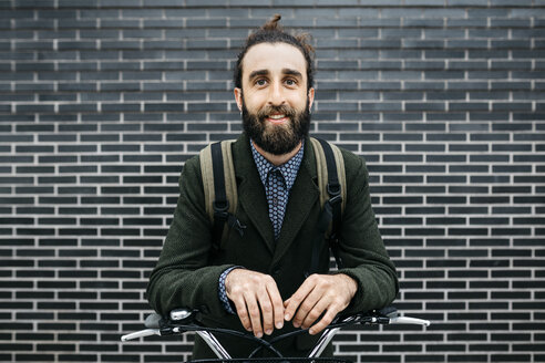 Porträt eines lächelnden Mannes mit E-Bike an einer Backsteinmauer - JRFF02961