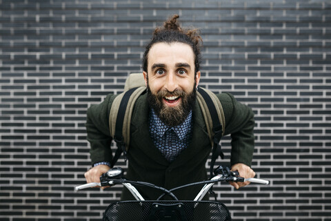 Porträt eines glücklichen Mannes mit E-Bike an einer Backsteinmauer, lizenzfreies Stockfoto