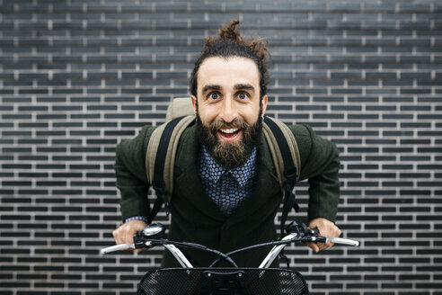 Porträt eines glücklichen Mannes mit E-Bike an einer Backsteinmauer - JRFF02962