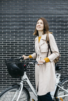 Lächelnde Frau mit E-Bike an einer Backsteinmauer - JRFF02964