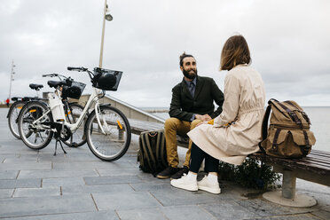 Paar sitzt auf einer Bank an der Strandpromenade neben E-Bikes und unterhält sich - JRFF02970