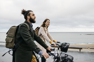 Couple riding e-bikes on beach promenade - JRFF02971