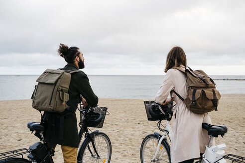 Paar mit E-Bikes am Strand mit Blick auf das Meer - JRFF02972