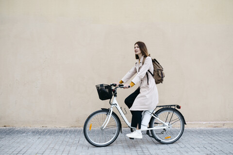 Frau fährt E-Bike entlang einer Mauer, lizenzfreies Stockfoto