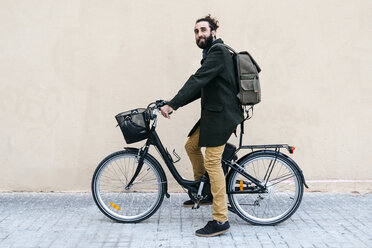 Portrait of smiling man with e-bike at a wall - JRFF02976